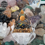 Orgonite Pyramidale de 6 cm de Côté en Résine avec des Pépites en Obsidienne Noire et 1 Boule en Œil de Tigre, du Métal et un Décor Arbre de Vie sur 1 druse en cristal
